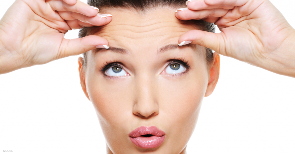 A woman looking up lifts her eyelids with her hands and wonders if nonsurgical eyelid treatments actually work.