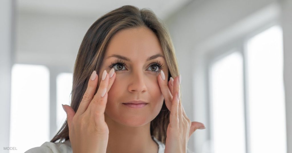 Woman (model) holds hands up to her face under her eyes,