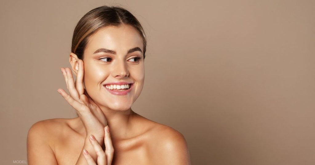 Woman with beautiful skin smiling and delicately touching the side of her face (model)