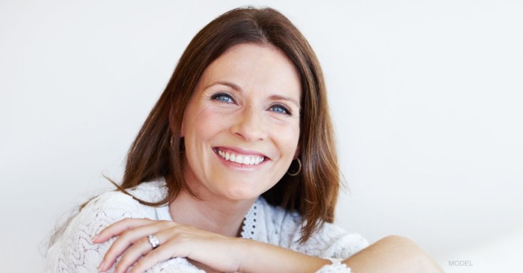 A woman looking forward smiling with dark brown hair and fair skin who has her arms folded across in front of her. (model)