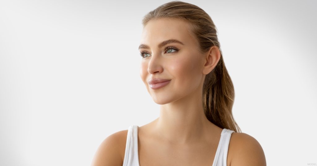 Smiling woman looking to the side, highlighting ponytail facelift results (model).